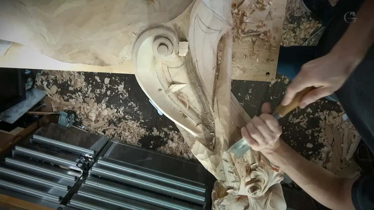 Two hands on a wide gouge in the long curved channel, with the scroll at the top of the frame