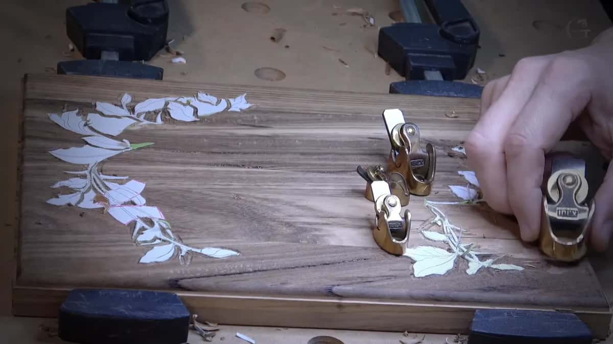 One hand lifts a brass plane off the board