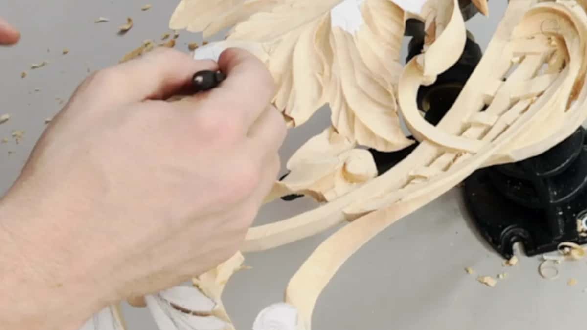 Hand and tool among carved leaves and curving bands