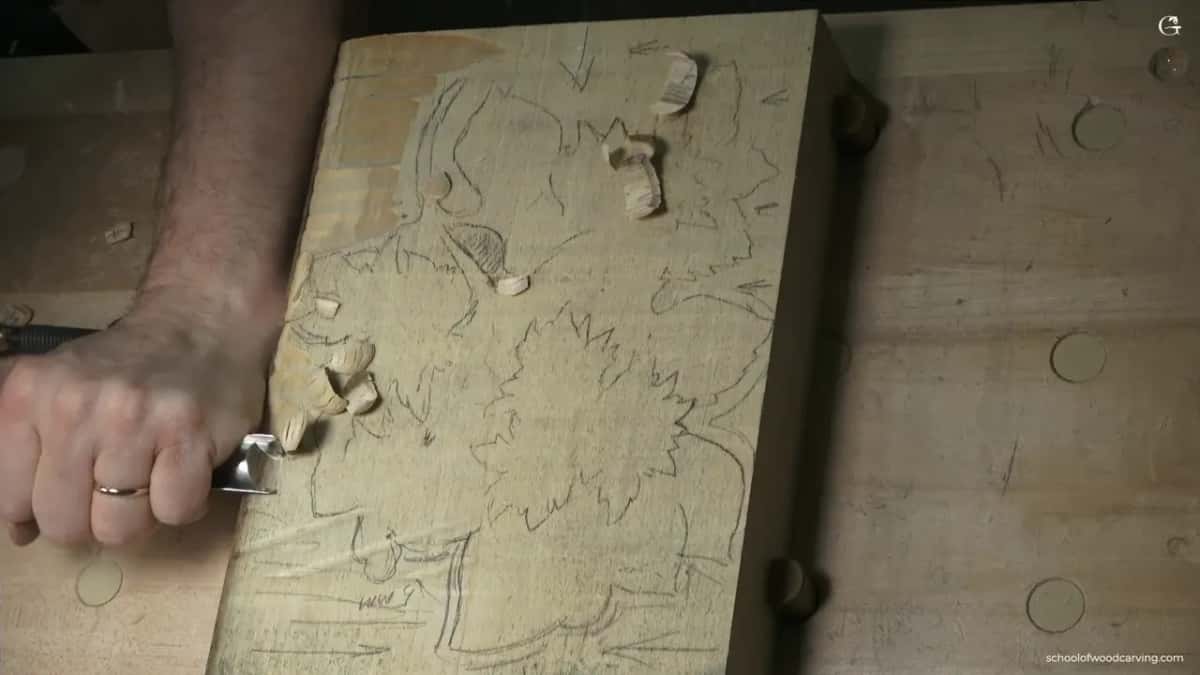 Hand drives a gouge along the top edge, chips scattered over the panel