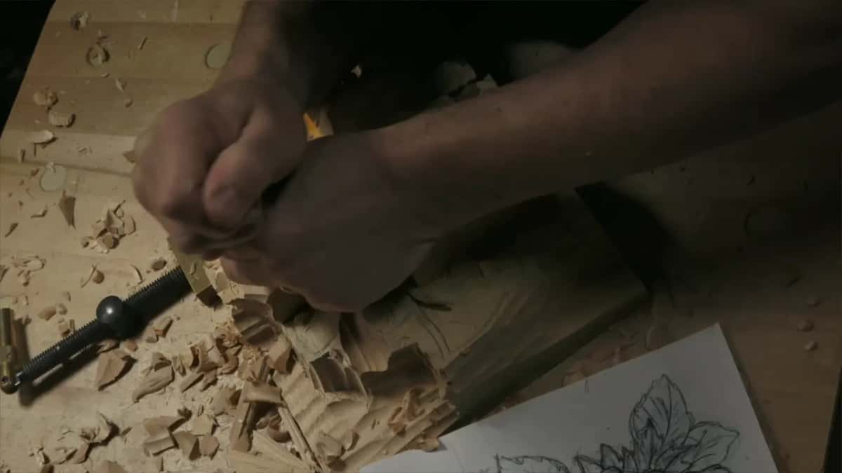 Two hands bear down on one small tool, a drawing of leaves and nuts on the bench below them