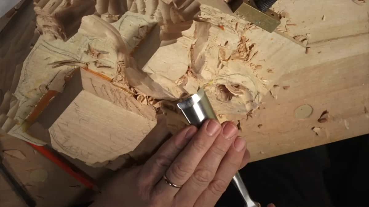 A wide gouge pressed to the wood under four fingers