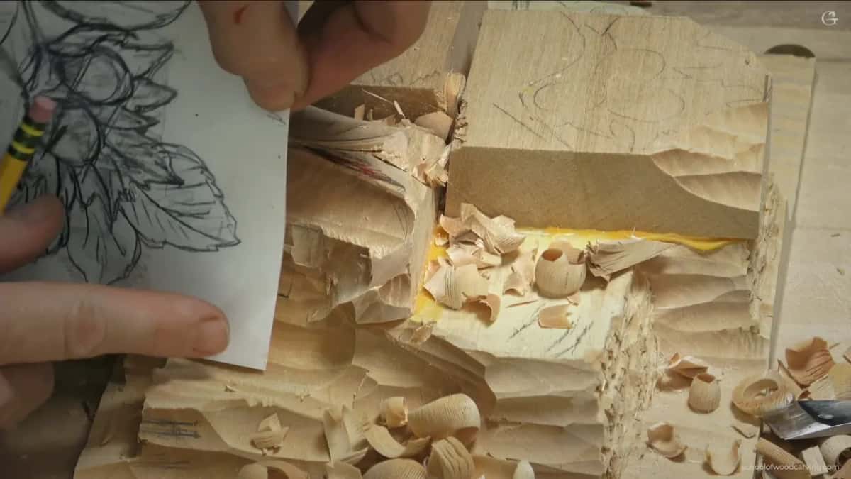 Paper pattern held up against the side of the carving, with a yellow pencil resting along its edge