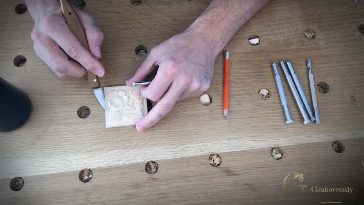 Knife tip on the border of the rosette while four punches and an orange pencil wait on the bench