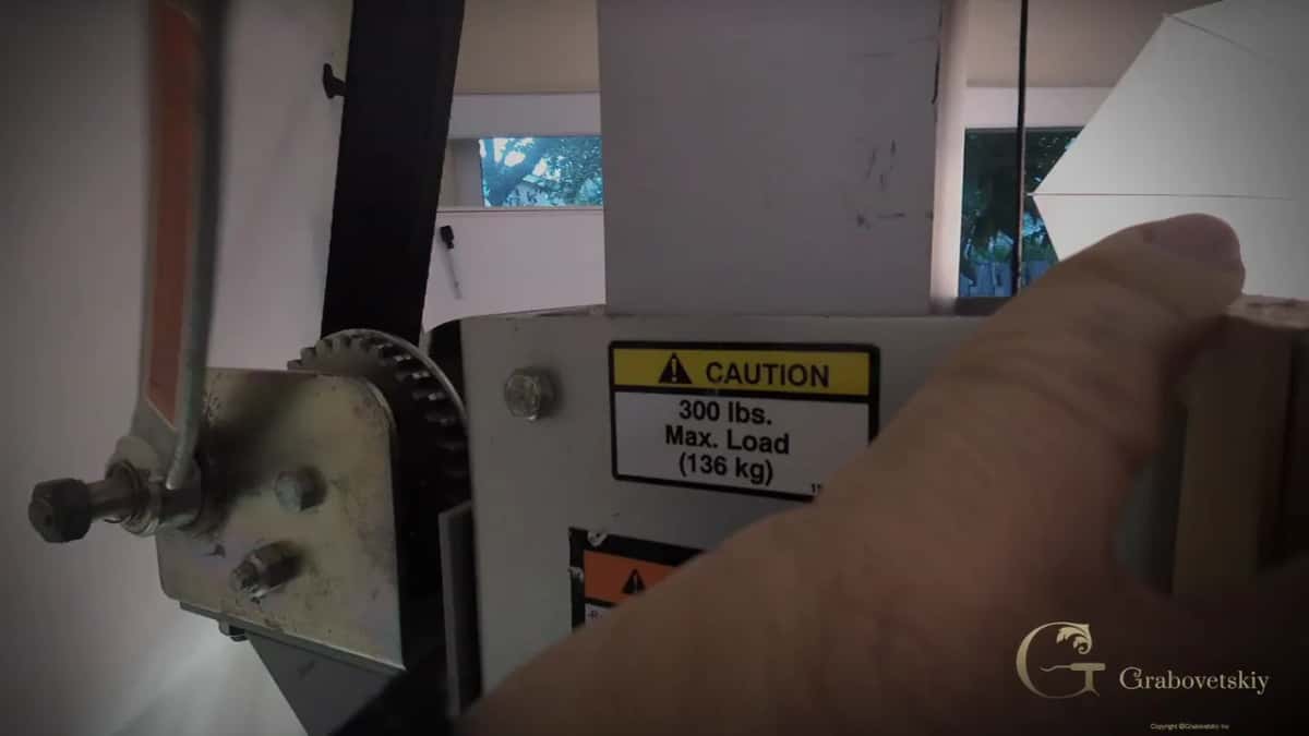Crank and toothed wheel on the lift beside a yellow caution label, 300 lbs. max load