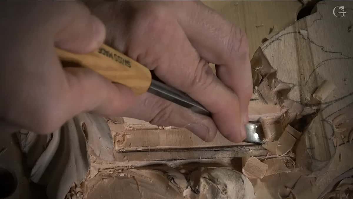 A flat tool held low on the molding band, shaving a pale floor with chips curling off its edge