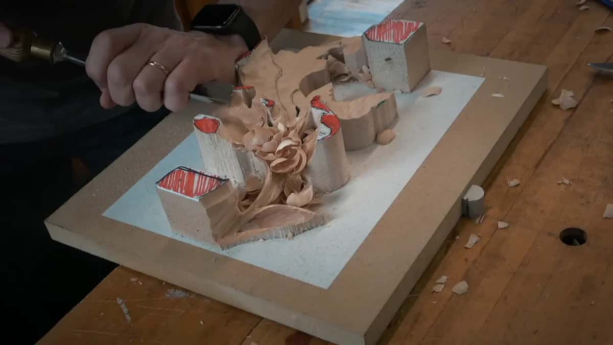Top down, a carving gouge scoops a hollow while red tabs hold the leaf