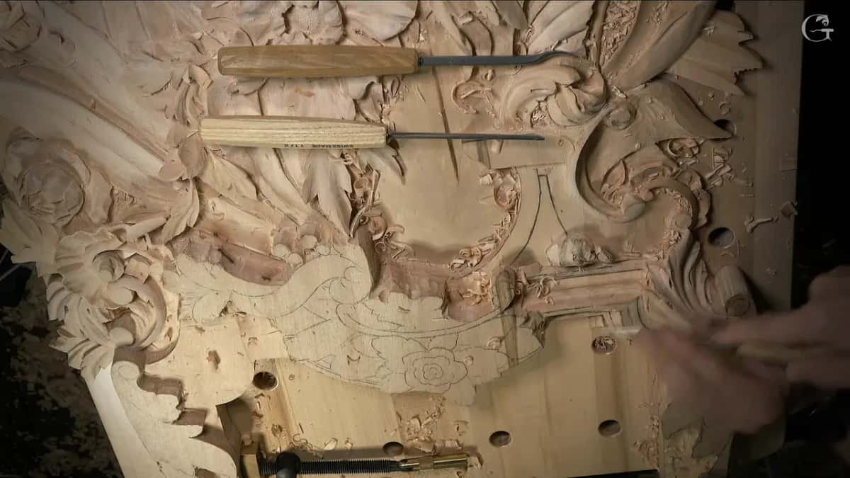 Two carving tools rest across the top of the panel while a hand moves below