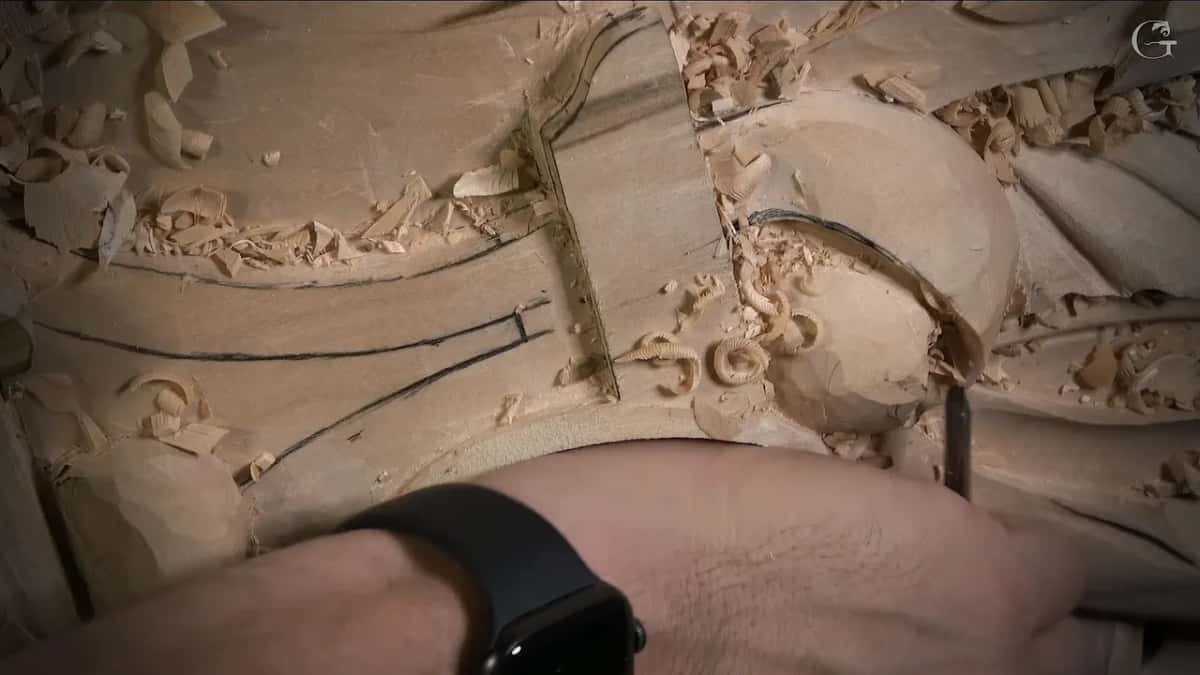 Small tool held upright at the curl, a black watch on the wrist
