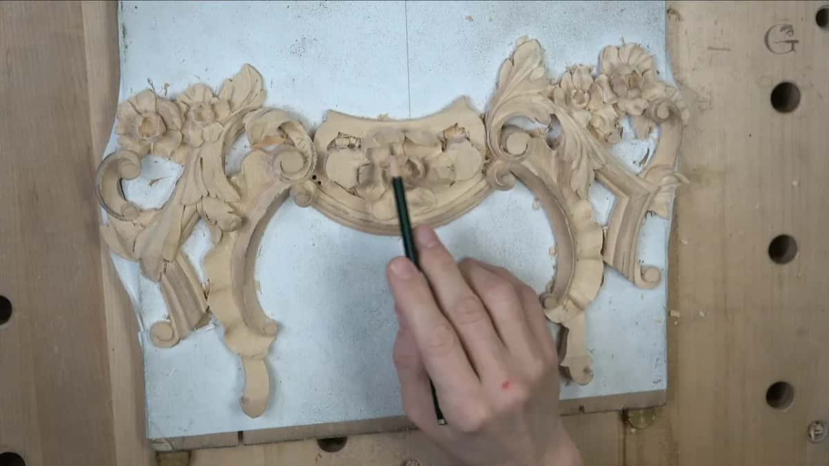 Pencil over a carved floral panel, still bare wood, resting on a white board