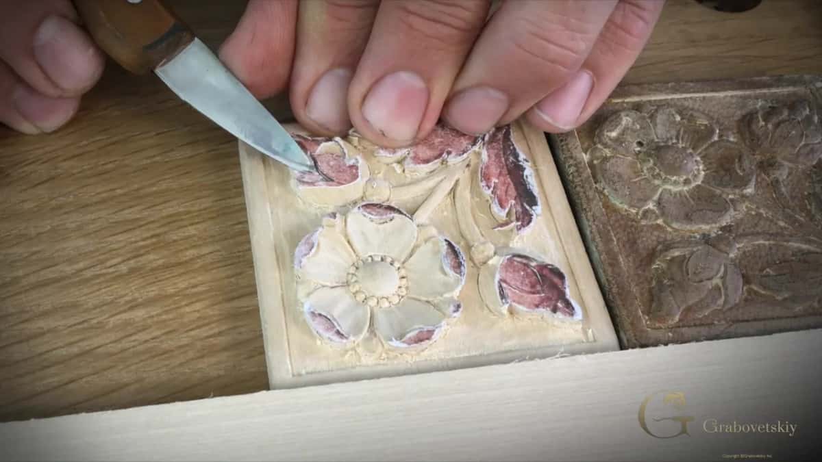 Wood handled knife held low against a small bud while one fingertip pushes the blade along from behind