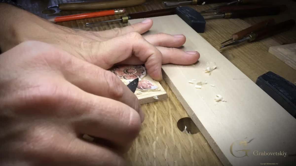 Both hands over the block, a pale board running beside it and carving tools lying behind.