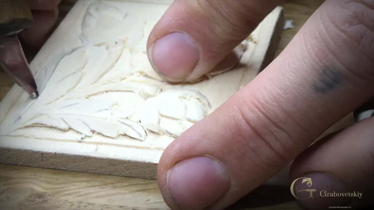 Tip of the knife sits in a line on a carved leaf, the flower above it and fingers pressing the block down.