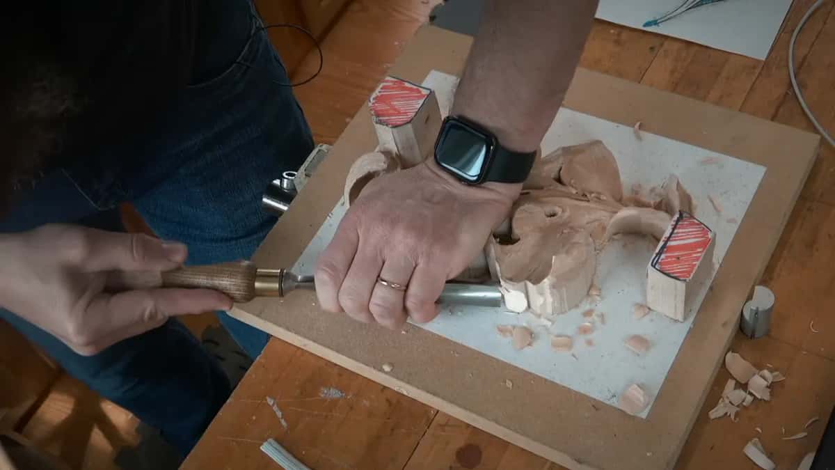 With one hand flat on the carving, the other guides a gouge toward the middle from the side