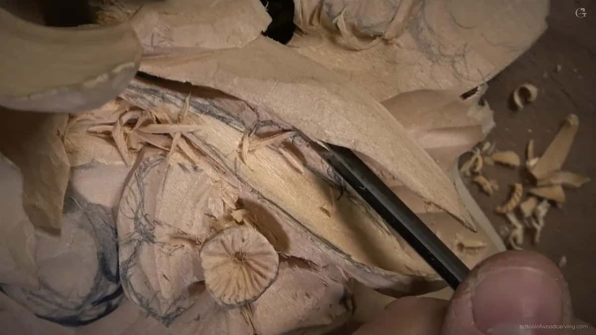 Narrow gouge slides under a leaf edge, shavings heaped beside it