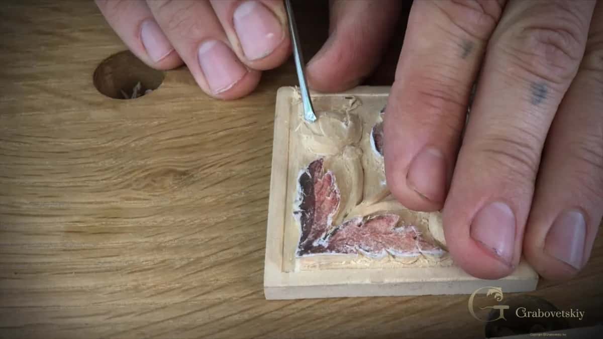 Fingers steady the block while a thin tool rounds the grooves of the small flower in the upper left corner