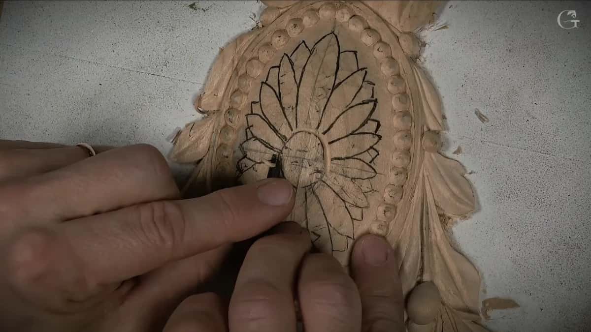 Fingers hold a small gouge on the black petal drawing inside the ring of beads