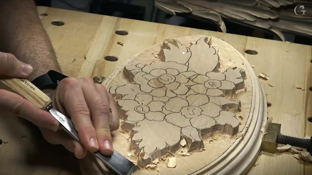 Flat gouge working inside the routed oval rim, chips piled along the edge