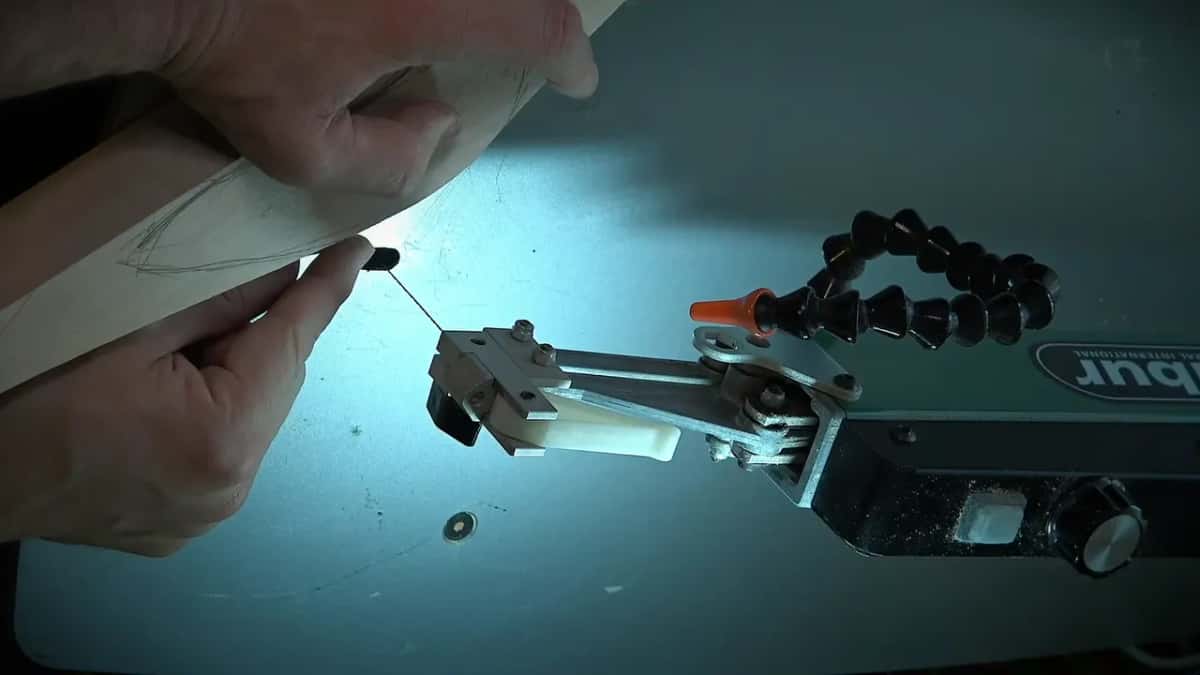 Fingertips steady a board beside the scroll saw blade under its upper arm