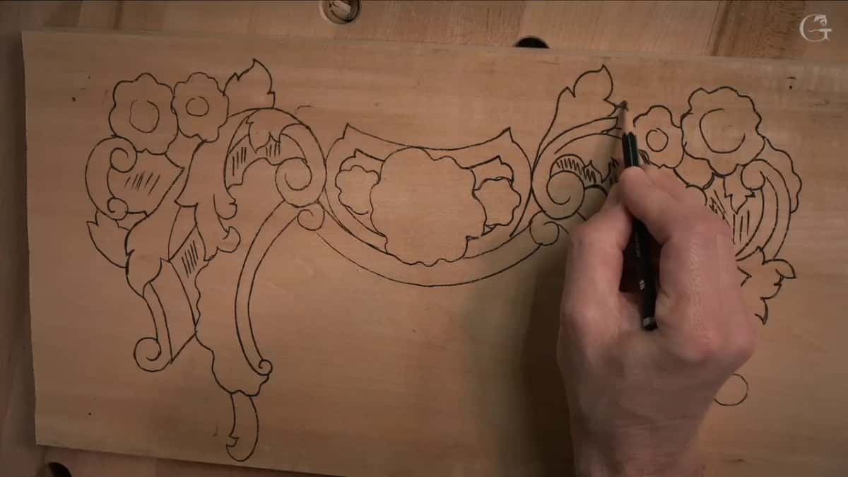 A pen rests on an inked scroll of the pattern, the board flat on the bench