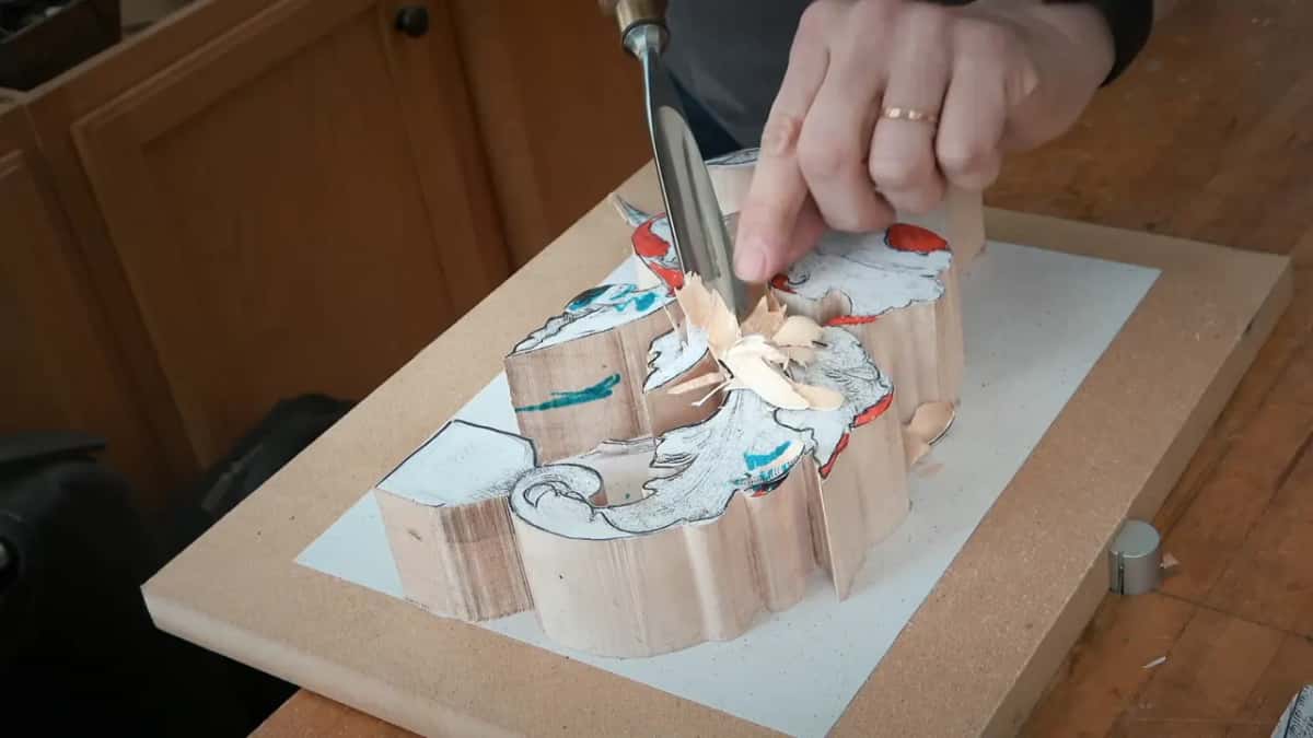 Curled chips lift from a paper-covered acanthus block as the gouge moves through the center