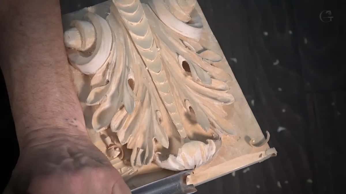 A forearm rests across a Roman acanthus leaf while the gouge lowers the background below it