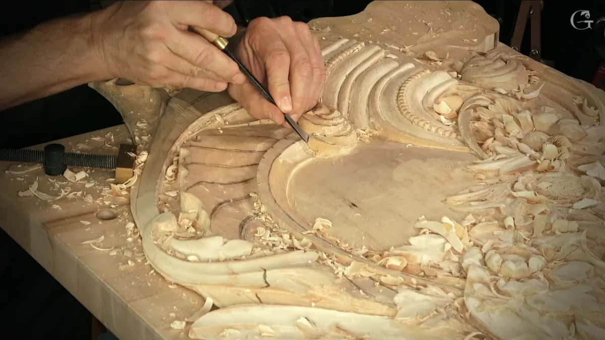 Two hands guide a slim tool round a curve on a big panel, a beaded border beside it and a bar clamp in the corner