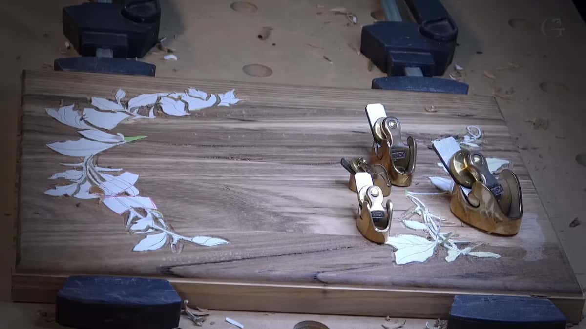 Four small brass planes sit on a dark board with white paper leaves on it and clamps at both ends