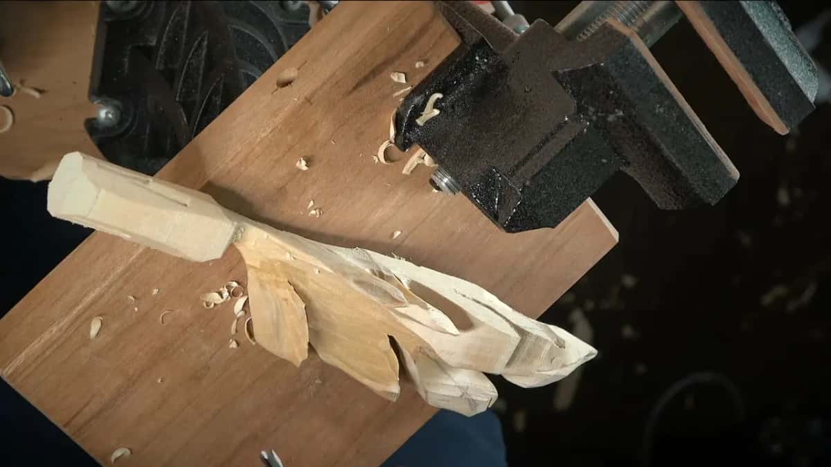 Carved leaf clamped in a vise on a board, with chips scattered around it