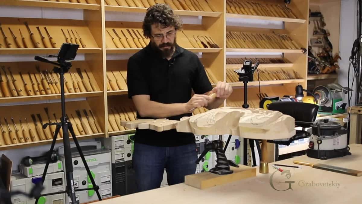 Both hands on a carving tool at the edge of a roughed-out piece