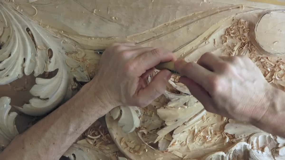 Between acanthus leaves, both hands close on the gouge, a yellow strip along the top