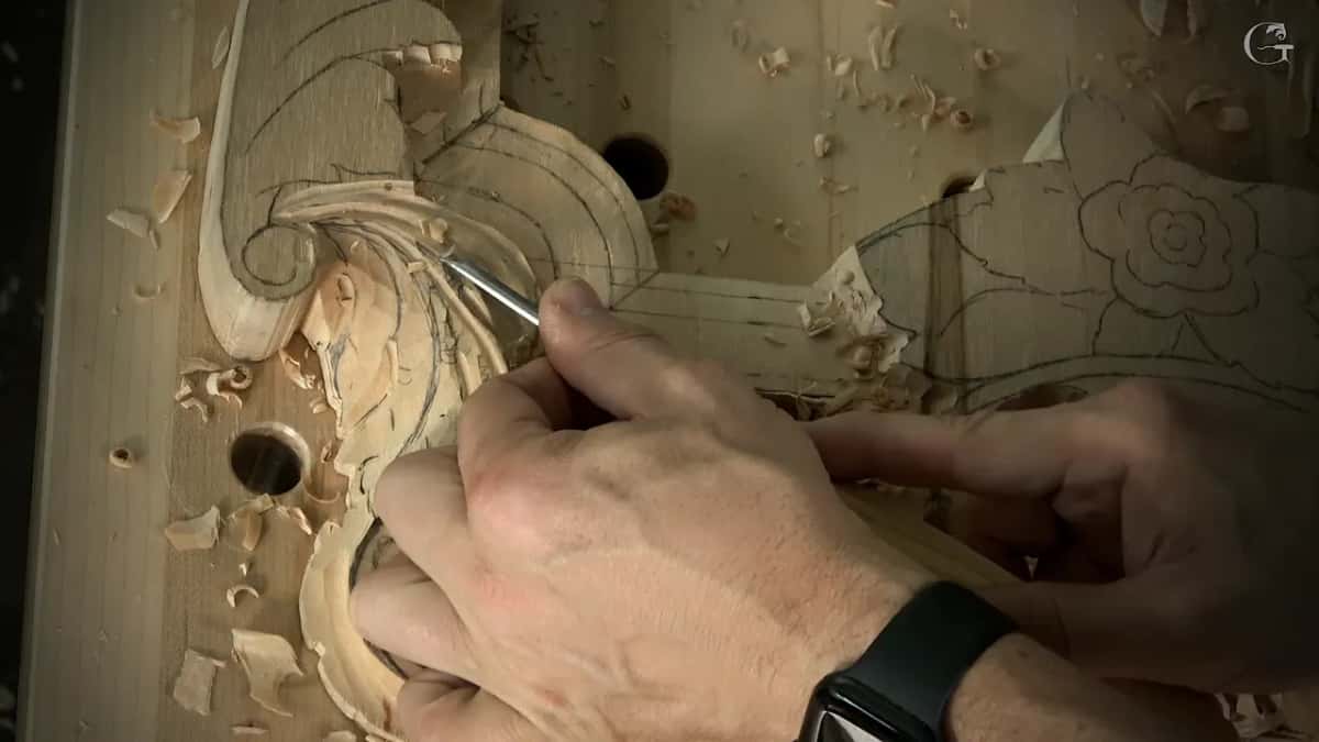 Close view of a hand with a black watch carving the leaf while the other hand braces the tool
