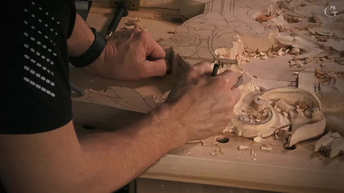 Side view of a forearm and both hands drawing lines with a pencil, chips scattered on the bench top