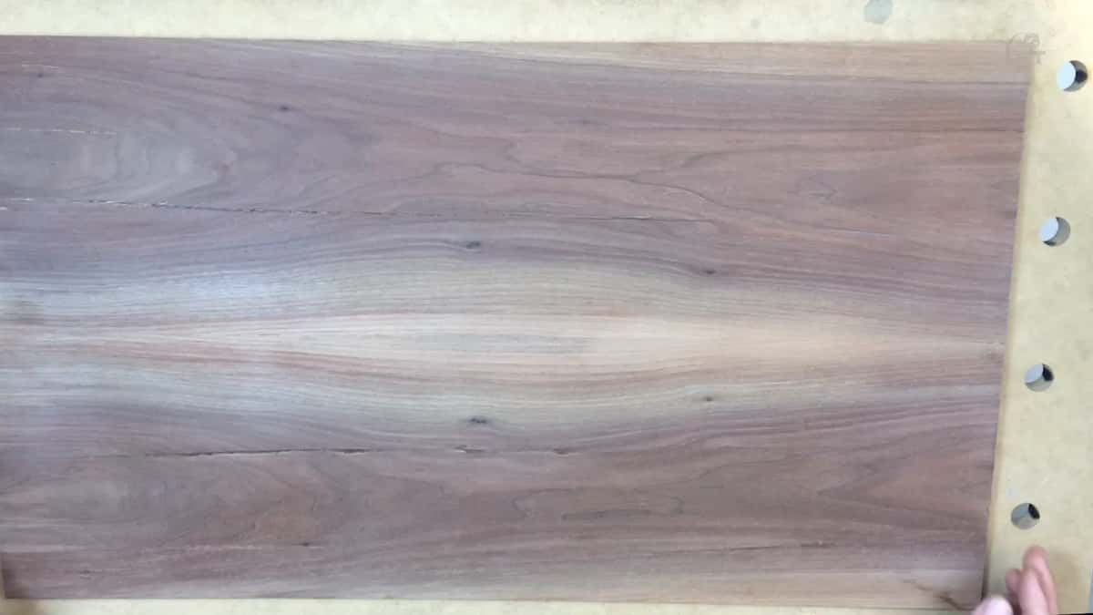Bare purple walnut board lying on a bench with round holes, dark streaks running along its grain