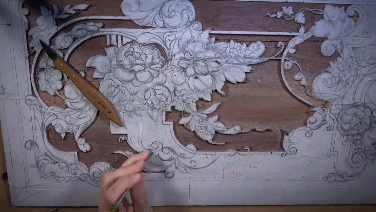 Fingers guide a long, thin tool along the edge of the bouquet on the walnut panel