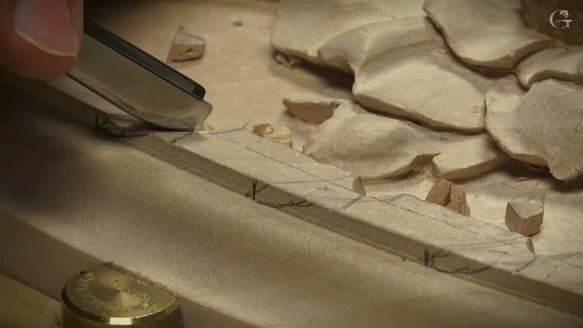 The gouge works along one pencil arch while small chips gather on the panel next to the carving