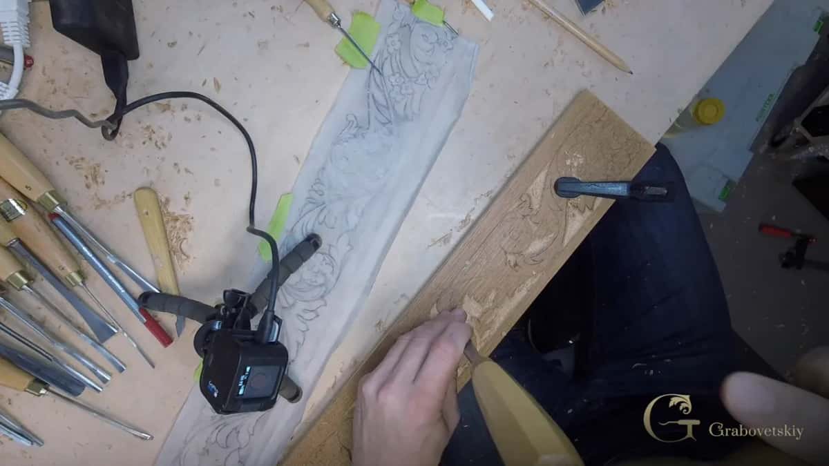 Looking down, one bench holds a long carving strip, a row of gouges, a small camera and a drawing