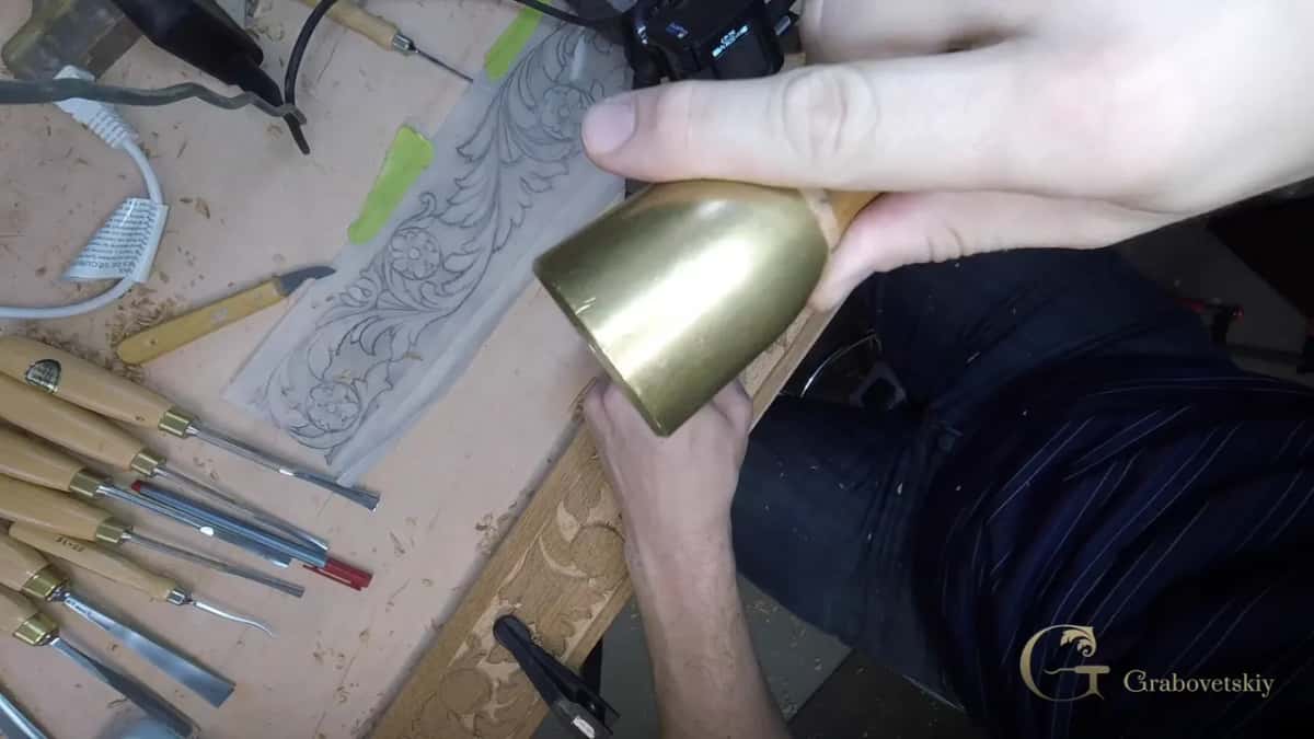 A brass mallet held over the bench, gouges lined up beside a pencil drawing on a clear sheet
