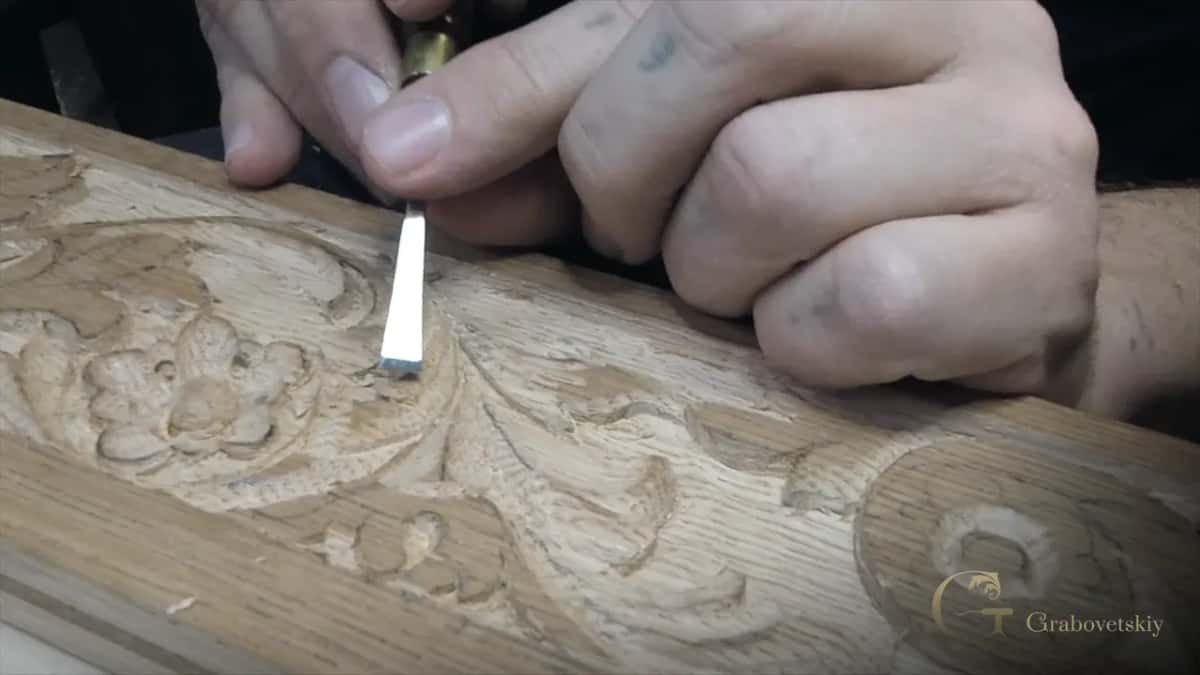 Clenched fist steadying a narrow flat chisel beside a carved flower