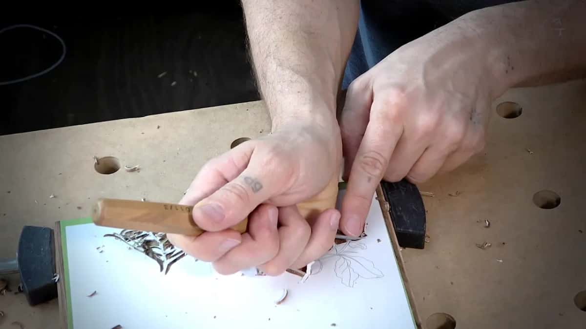 Both hands on one short handle, low over a paper pattern of leaves, with black clamps at its sides