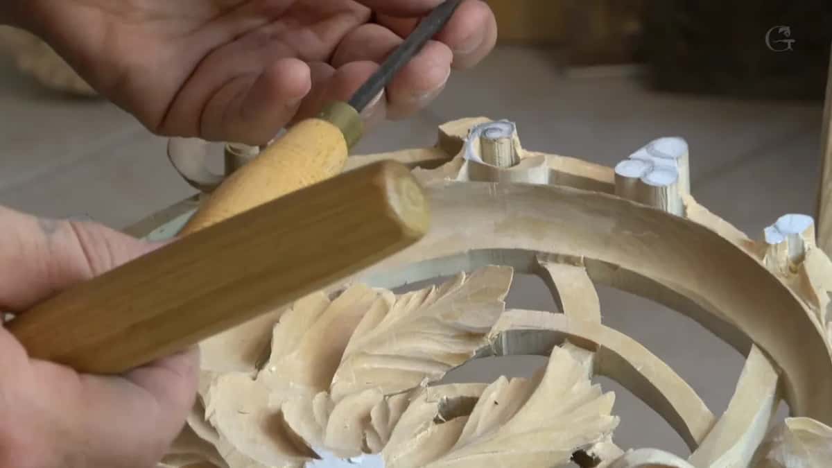 An octagonal handle, held in two hands above a ring of carved leaves and ribbons.