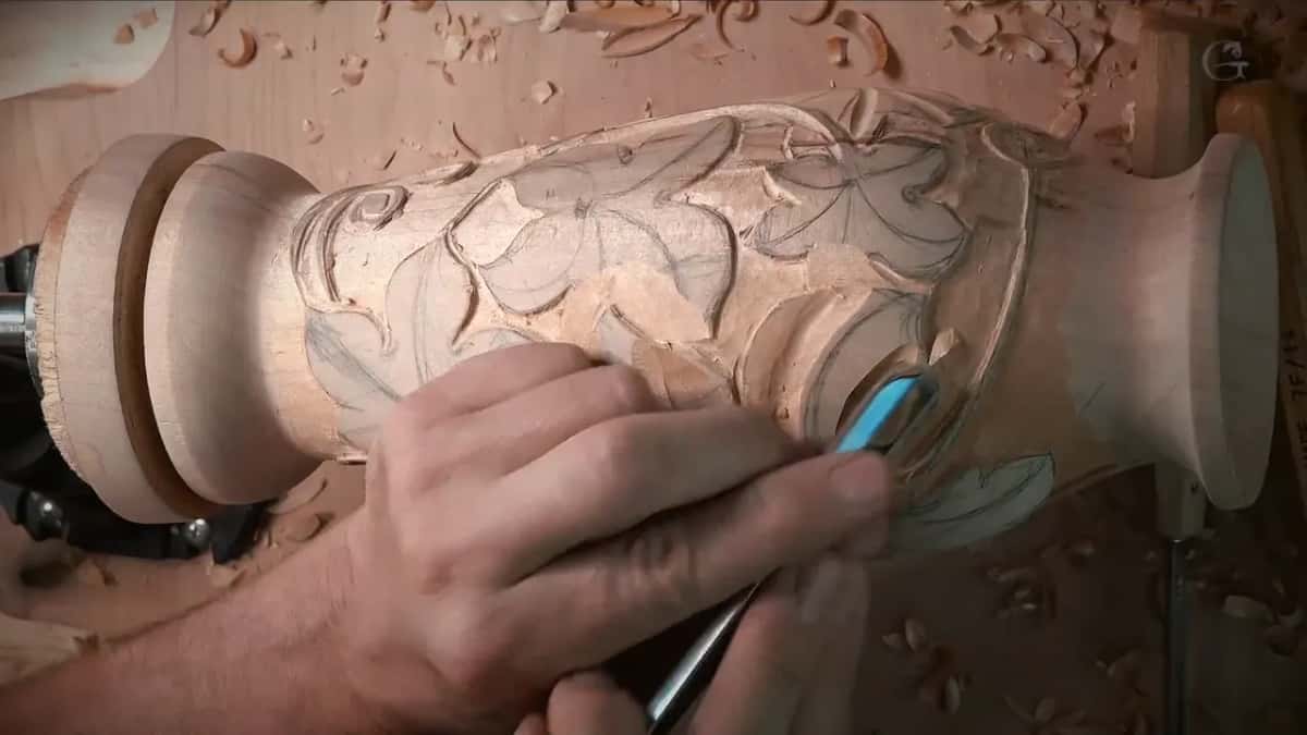 Hands work a tool along the leaves while shavings lie on the bench