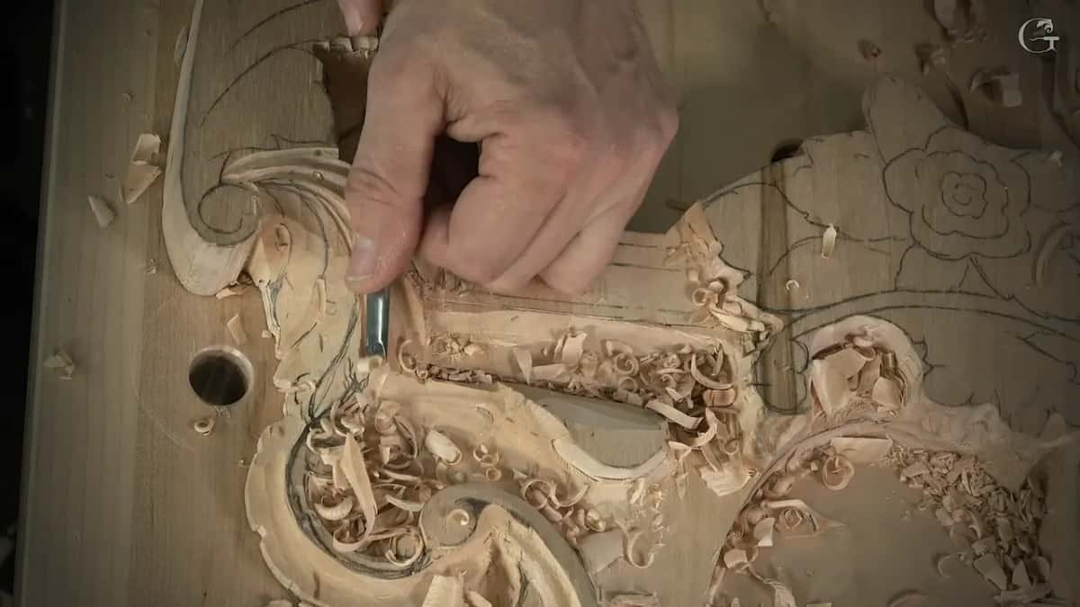 Fingers steady the shank while a slim tool runs down the leaf toward the scroll
