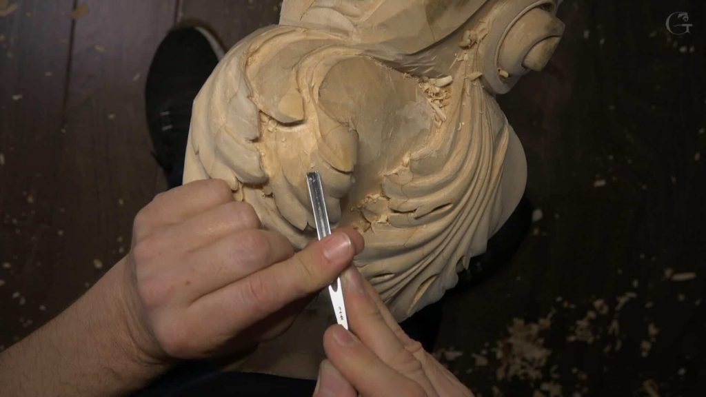 Person carefully carving intricate details on a wooden sculpture using a chiseling tool. This scene reflects the focus and skill involved in wood carving classes and lessons, as the artist shapes the wood with precision.