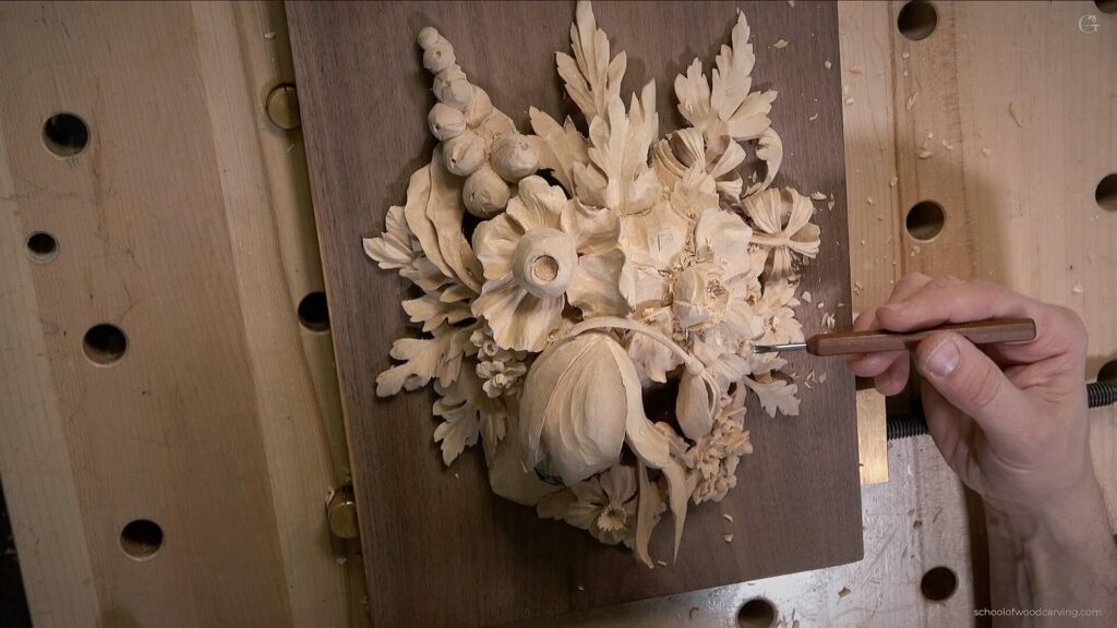 A close-up of a wood carving in progress, featuring a detailed floral design on a wooden panel. A hand is shown skillfully using a carving tool to create lifelike flowers and leaves, with wood shavings scattered around. This image captures the essence of wood carving classes, demonstrating the craftsmanship and creativity involved in wood carving lessons.
